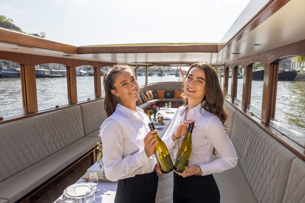 Twee serveersters met een fles wijn in hun handen op een diner rondvaart Amsterdam.