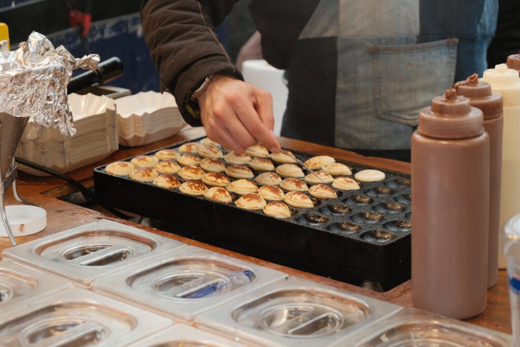 A person making poffertjes in a special pan.