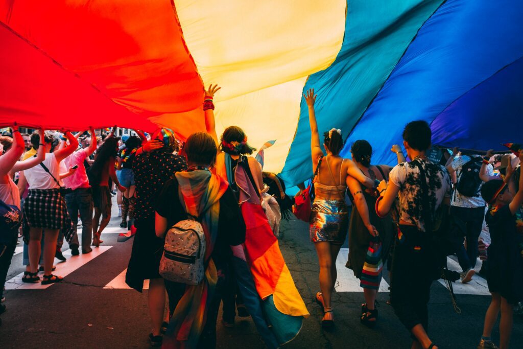 People walking under a rainbow flag during Amsterdam Pride. 